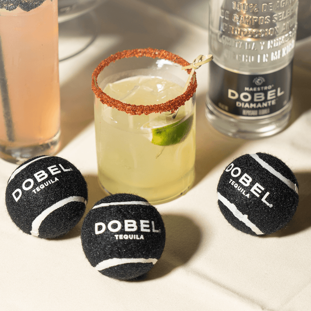 Black Dobel tennis balls on a table with a Dobel margarita cocktail.