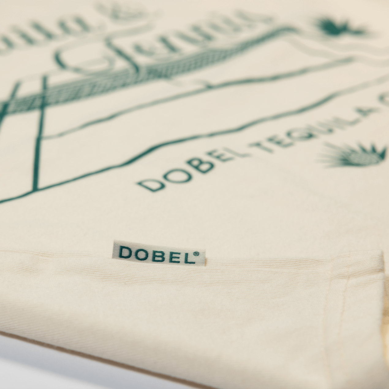 Close up detail shot of cream mid-crop shirt with large "Tequila & Tennis" graphic.