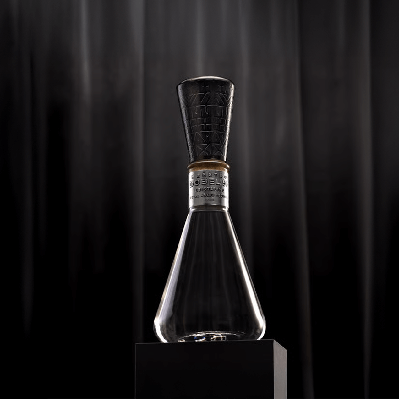 Dobel 50 Cristalino Onora Laca de Olinala elegant bottle on a black pedestal.