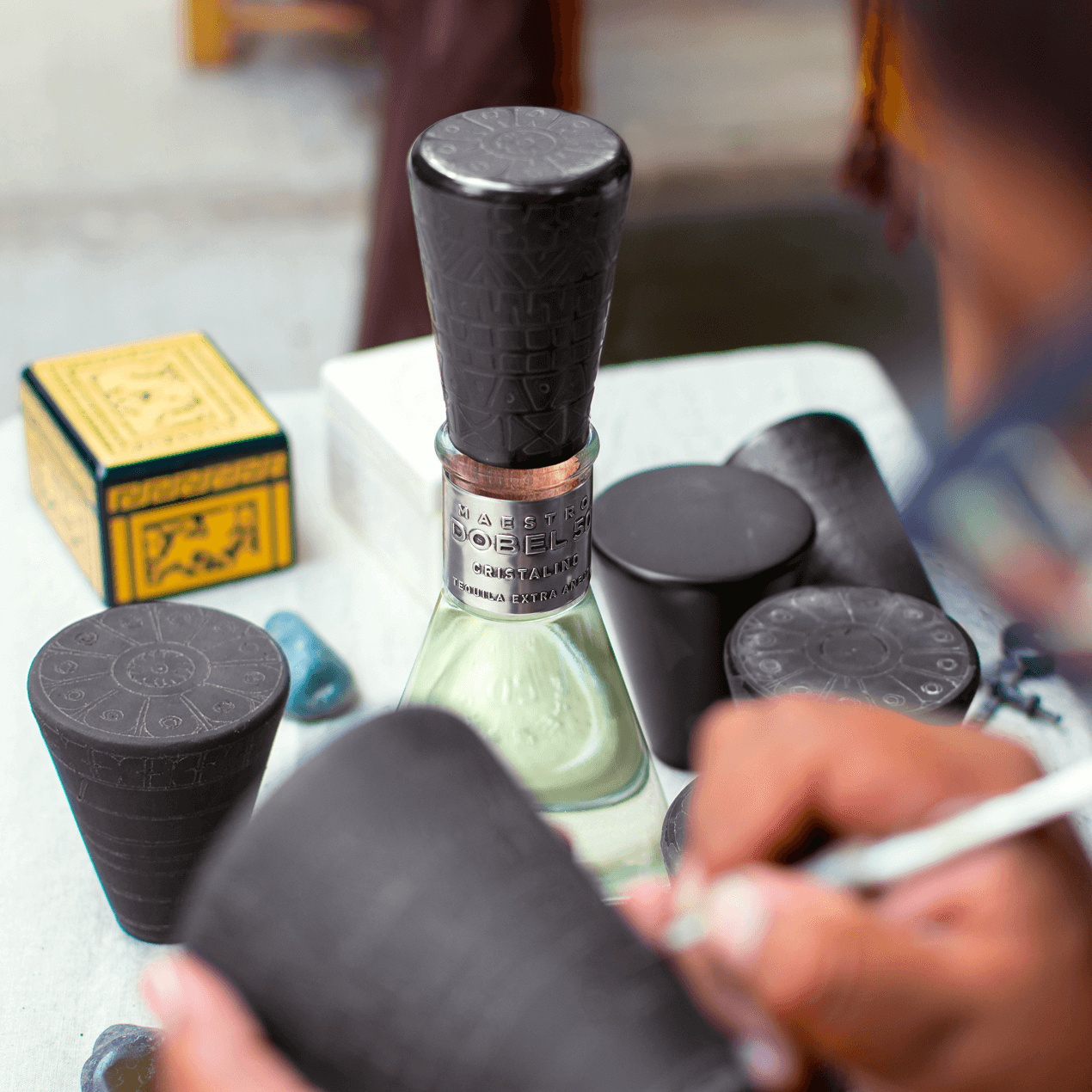Dobel 50 Cristalino Onora Laca de Olinala bottle with cap and artistic tools on a table.
