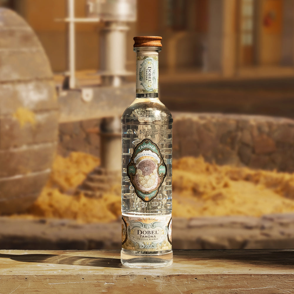 Dobel Tahona stands on a wooden surface with a rustic distillery background.