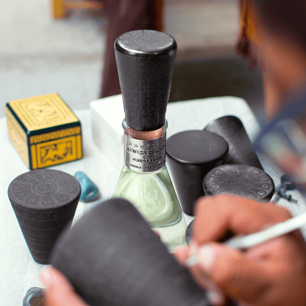 Dobel 50 Cristalino Onora Laca de Olinala bottle with cap and artistic tools on a table.