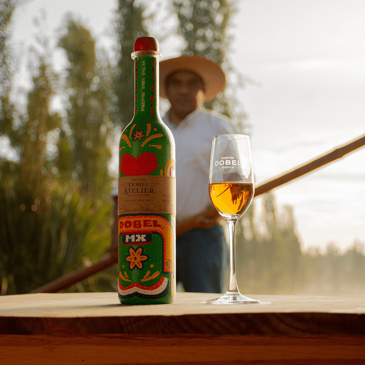 Dobel Atelier: Trajineras Edition bottle with a glass on a wooden surface outdoors.