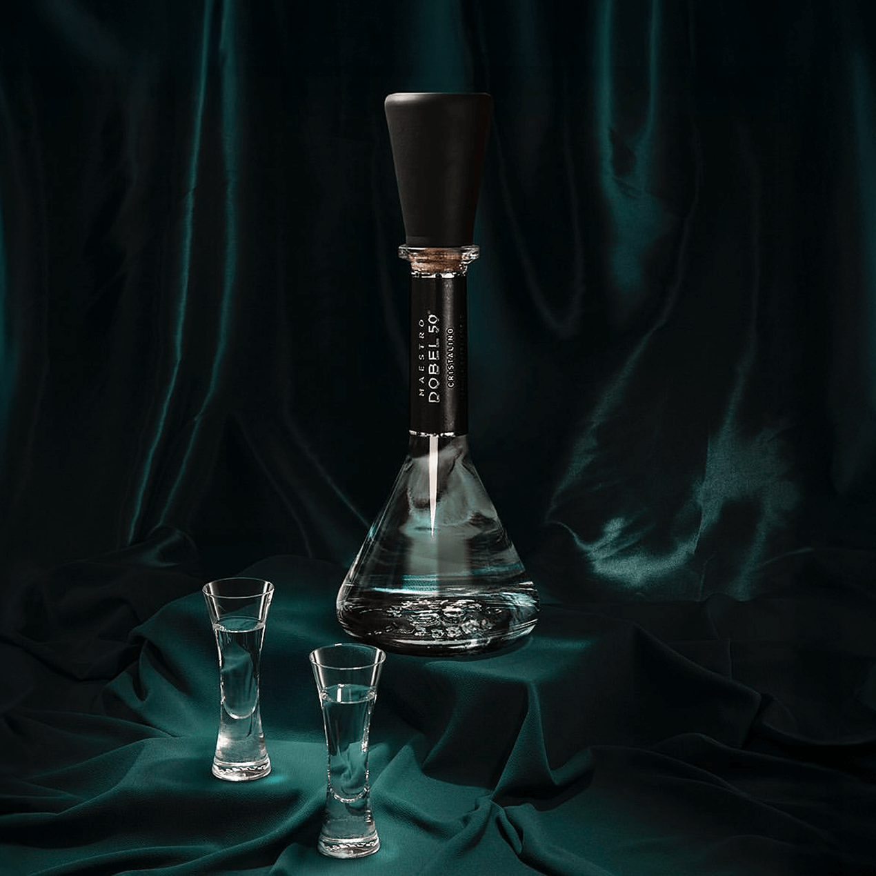 Two Dobel sipping glasses with Dobel 50 Cristalino bottle on a teal velvet fabric.